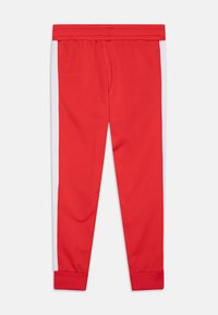 Red athletic pants featuring a white side stripe, elastic waistband, and ribbed cuffs. Made from a smooth, stretchy material.