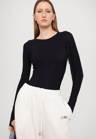 Black long-sleeve bodysuit with fringe detailing on sleeves, paired with white sweatpants featuring a small black graphic.