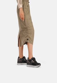 Scarpe da ginnastica nere con mesh testurizzato e dettagli, abbinate a una gonna leggera color khaki con coulisse e spacchi laterali.