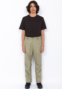 Sort crew neck t-shirt, løs pasform. Lysegrøn cargo bukser med justerbar talje, lynlås lommer og knapbuttons detaljer. Sorte sko.