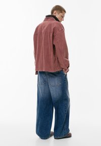 Czerwona kurtka z kordurowej tkaniny z czarnym kołnierzem, zestawiona z luźnymi niebieskimi dżinsami o gradientowym efekcie. Casualowy design z luźnym krojem.
