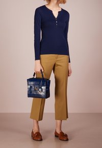 Mörkblå långärmad topp med krage och tre guldknappar, i kombination med bruna loafers och en mörkblå handväska med krokodilprägling och guldaccenter.