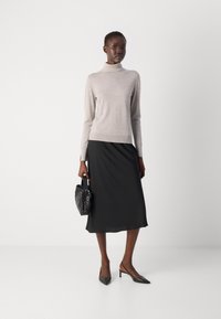 Lys beige turtleneck sweater, sort midi-nederdel, sorte stiletto-sandaler med peep toe og en lille struktureret håndtaske.