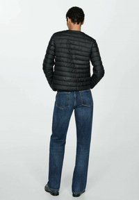 Zwarte gewatteerde jas met een ronde halslijn, een gestructureerd oppervlak en zichtbare stiksels, gecombineerd met blauwe recht model jeans.
