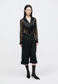 Transparent black button-up shirt with long sleeves, paired with black cropped trousers. Features a belted waist and pointed heels.