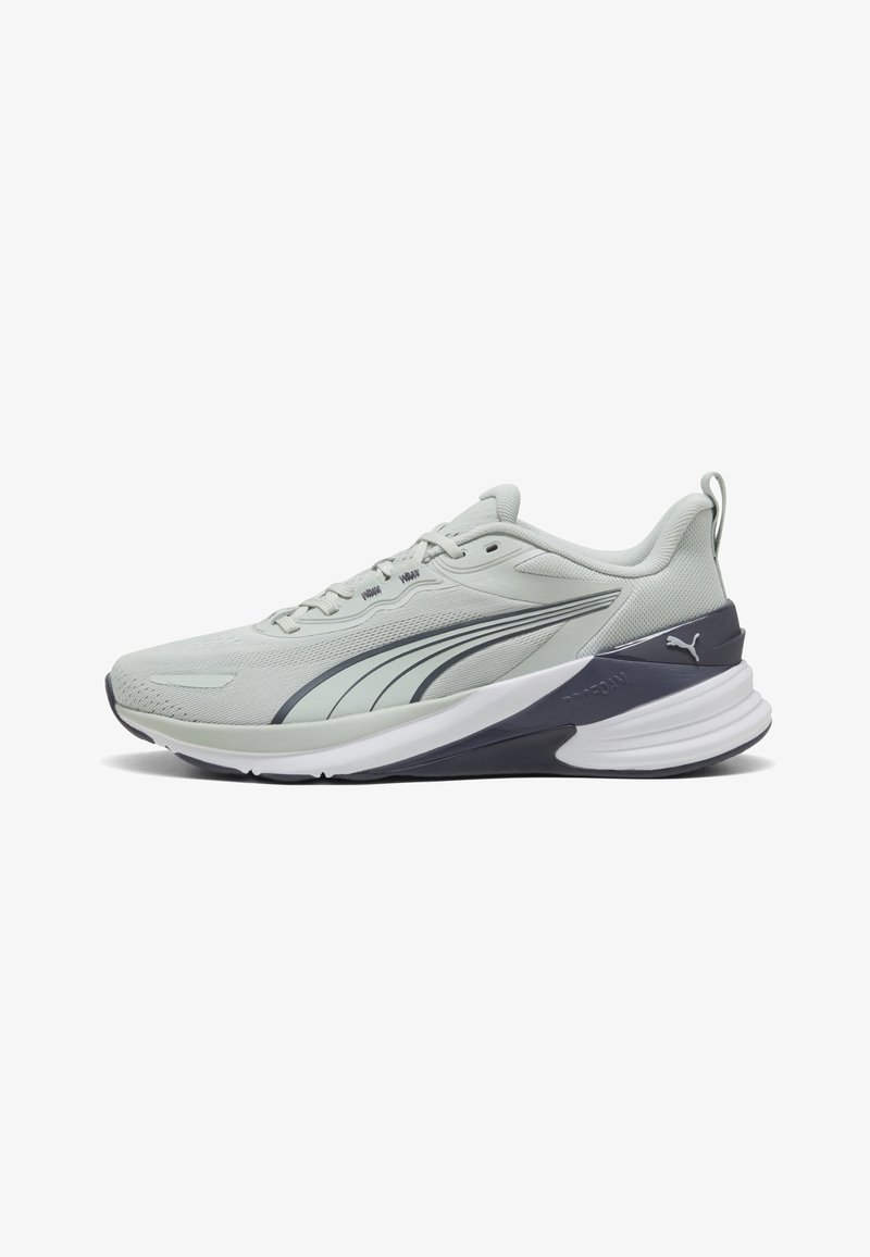 Ανοιχτό γκρι αθλητικό παπούτσι Puma με σκούρες γκρι λεπτομέρειες, λευκή μαλακή σόλα και θηλιά στο πίσω μέρος, εμφανίζεται σε πλευρικό προφίλ.