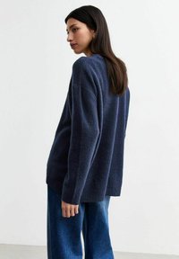 Pull bleu marine avec une finition texturée, arborant une coupe décontractée, des épaules tombantes et un col rond, associé à un denim à jambe large.
