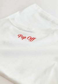 Biała bawełniana koszulka z czerwoną haftowaną grafiką "Pop Off". Okrągły dekolt, miękka tekstura i płaski krój.