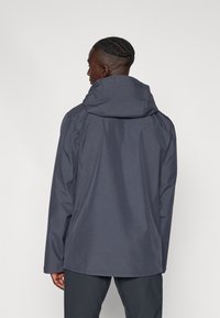 Jachetă impermeabilă de culoare navy, cu guler înalt și glugă, având o croială lejeră și o textură netedă, concepută pentru utilizare în aer liber.