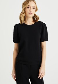 Zwarte top met korte mouwen in een ribbelstructuur, ronde halslijn en iets prinselijke mouwen. Zachte stof en een ontspannen pasvorm met een tailleband.