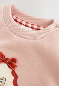 Jersey rosa acanalado con cuello redondo, con cuello interior de cuadros rojos y blancos y un pequeño botón cerca del hombro.