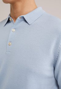 Polo shirt tricotat de culoare albastru deschis, cu guler, încheiere cu trei butoane și mânici cu nervuri, având o textură subtilă pe material.
