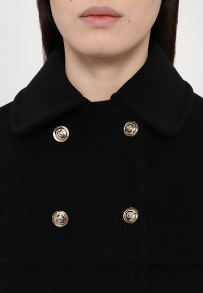 Black wool coat with a large collar, featuring gold-tone button closures and a smooth texture. Notable for its structured design and classic style.