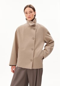 Beige wool blend jacket, featuring a high collar, five-button closure, and oversized, structured silhouette. Smooth texture and relaxed fit.