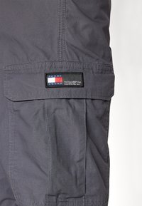 Šedé cargo šortky vyrobené z lehkého materiálu. Na kapse mají obdélníkovou nášivku Tommy Jeans v červené, bílé a modré barvě.
