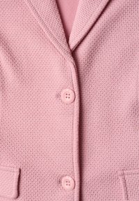 Gros plan d'un blazer rose texturé avec revers, deux grands boutons assortis et petites poches à rabat.