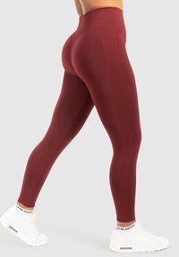 Burgundy högmidjade leggings med en slät textur, åtsittande design och sömlös konstruktion, parat med vita träningsskor.