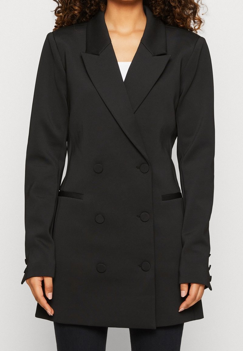 Blazer noir à double boutonnage avec une coupe cintrée, revers crantés, deux poches avant et des accents de bouton sur les poignets. Texture de tissu lisse.