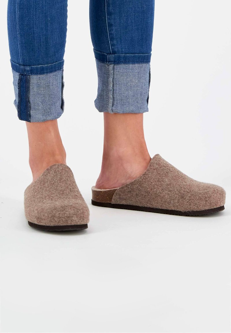 Braune Filzschuhe mit einer glatten Textur und abgerundetem Vorderteil, kombiniert mit hochgekrempelten blauen Jeans aus Denim, die unter dem Umschlag einen kontrastierenden helleren Stoff aufweisen.