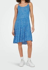 Sininen kukkamekko, jossa on spagettiolkaimet, levenevä hame ja kevyt kangas. Yhdistettynä valkoisiin tennareihin ja nilkkasukkia.