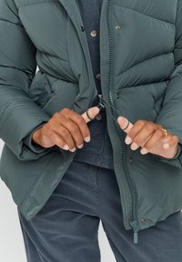 Dark green puffer jacket with a textured finish, zip closure, and ribbed cuffs, worn over a navy ribbed top and corduroy pants.