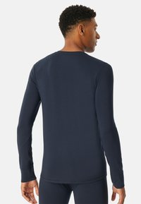 Camicia a maniche lunghe di un blu marino scuro, realizzata in tessuto morbido. Presenta un collo rotondo e un design aderente, con polsini allungati ai polsi.