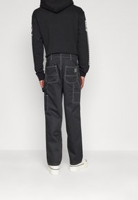 Czarne spodnie cargo z kontrastową białą nicią, wieloma kieszeniami i luźnym krojem. Połączone z czarną bluzą z kapturem i białymi sneakersami.