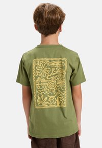 Green cotton t-shirt with a large yellow floral and abstract pattern printed on the back. Short sleeves and a classic crew neck design.