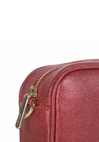 Bolso metálico rojo con cremallera presenta una superficie texturizada, herrajes dorados y bordes redondeados, exhibiendo un diseño elegante y acentos funcionales.