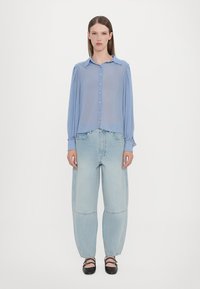 Light blue sheer button-up shirt with a collar and button placket, paired with oversized light blue jeans. Simple black shoes complete the look.