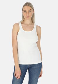 Witte geribde tanktop met een ronde halslijn en brede bandjes, getailleerde vorm, gecombineerd met blauwe jeans, op een effen achtergrond.