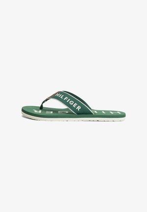 Grüne Tommy Hilfiger Flip-Flop mit weißer Sohle und Stoffriemen mit der Aufschrift „HILFIGER“, in Seitenansicht dargestellt.