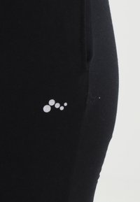 Leggings neri realizzati in un tessuto liscio presentano un piccolo motivo circolare bianco sul lato inferiore. Il design è semplice e uniforme.