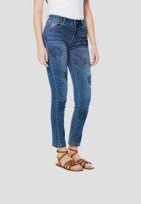 Blauwe spijkerbroek met bloemenborduursel in marineblauw, aansluitend model en enkellange snit, gecombineerd met bruine sandalen met bandjes.