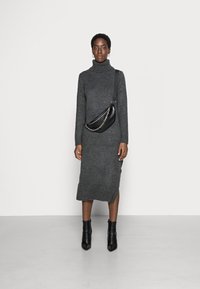 Vestito midi grigio lavorato a maglia con colletto alto, dotato di uno spacco laterale. Borsa a spalla in pelle nera con dettagli in catena e stivaletti con tacco.