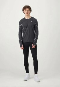 Camiseta atlética negra de manga larga con acentos blancos, combinada con leggings negros. La modelo lleva zapatillas blancas. El material parece elástico y ajustado.