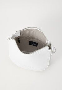 Bela usnjena torbica za ramo z zadrgo, gladke teksture, in notranjosti iz svetlo rjave tkanine, ki vsebuje majhen žep z zadrgo in oznako z logotipom.