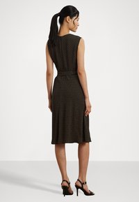 Black dress with a fitted bodice and A-line skirt, featuring a polka dot pattern in yellow and white. Worn with black high-heel sandals.