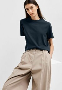 Dark navy short-sleeved t-shirt paired with light beige high-waisted, pleated trousers. Smooth fabric texture; relaxed fit.
