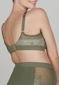 Olivgrüner, drahtloser BH mit einem Rückenpanel aus floraler Spitze und verstellbaren Trägern. Texturiertes Material mit Haken- und Ösenverschluss auf der Rückseite.