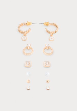 Hét pár aranyszínű bedugós és karika fülbevaló, melyeket virágmintás medálok, gyöngyök és áttetsző drágakövek díszítenek, fehér háttéren elrendezve.