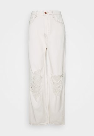 Kremowe dżinsy o szerokich nogawkach wykonane z denimu, z dwoma postrzępionymi łatami na kolanach, zapięciem na guziki z przodu oraz widocznymi detalami szwów.