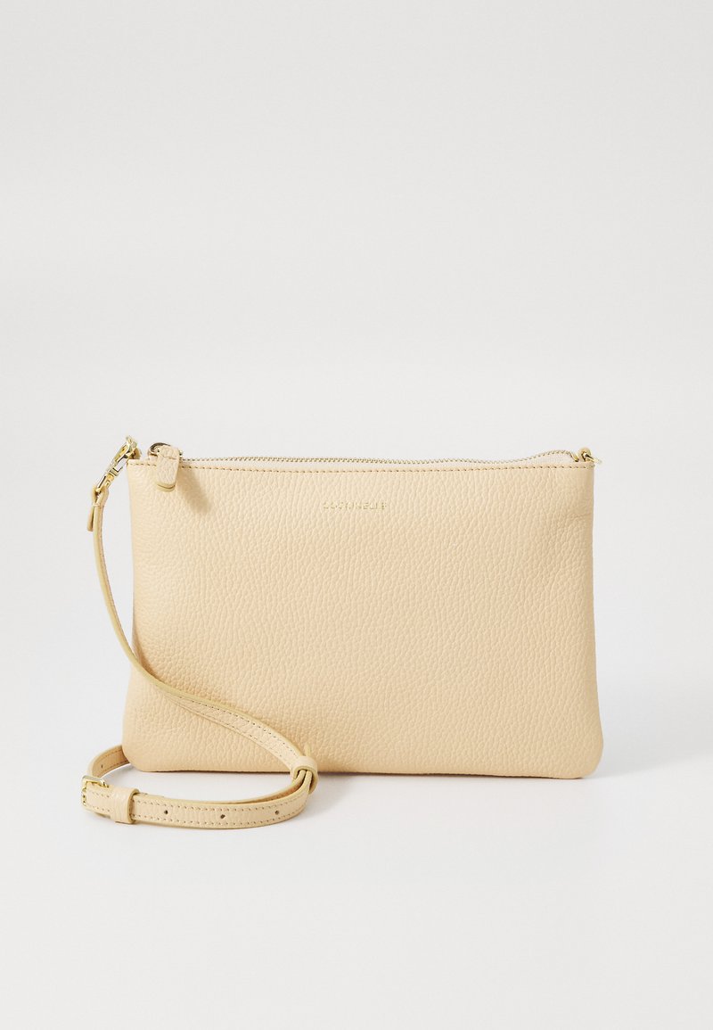 Pouch de pele bege com uma superfície texturizada, apresentando um fecho de zip na parte superior e uma alça ajustável para transporte. Branding minimal presente.