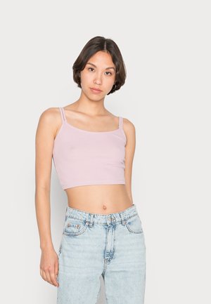 Top cropped de cor rosa claro, com textura canelada e alças finas, combinado com jeans claros desfiados, exibindo um look casual.