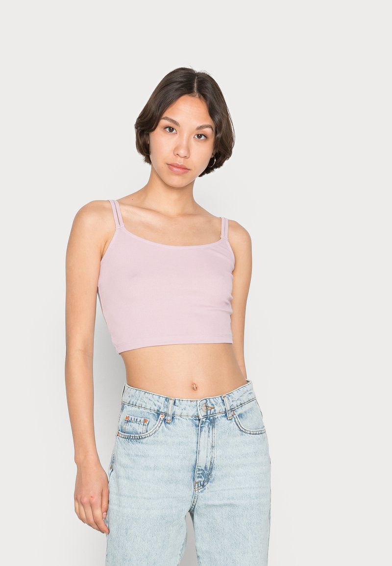 Top cropped de cor rosa claro, com textura canelada e alças finas, combinado com jeans claros desfiados, exibindo um look casual.