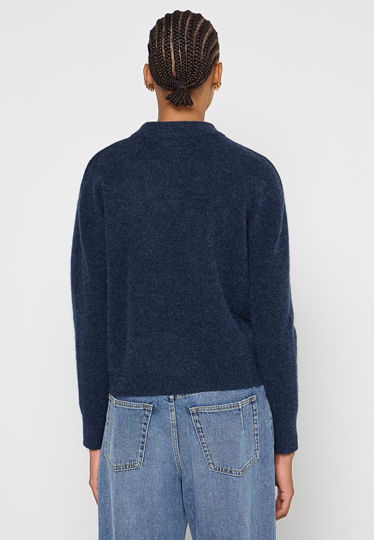 Navyblauer Wollpullover mit Rundhalsausschnitt und überschnittenen Schultern, getragen mit hellblauen Jeans aus Denim mit Gesäßtaschen und Nähten.