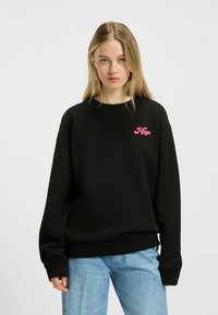 Felpa nera con logo rosa "Hugo" sul petto, caratterizzata da una vestibilità rilassata, colletto a girocollo e polsini e orlo a coste. Design casual.