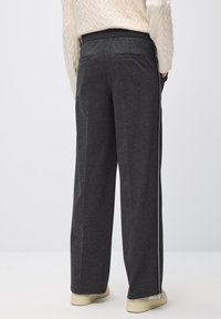 Pantalons larges gris foncé en tissu doux, dotés d'une taille élastique et de deux poches arrière. Des bandes blanches décorent les jambes.