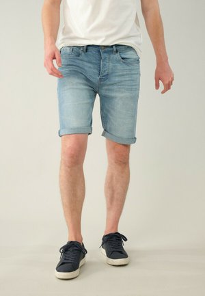 Shorts en denim bleu clair avec une finition délavée, des ourlets roulés et un design classique à cinq poches. Assortis à des baskets bleu foncé.
