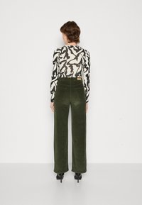 Groene corduroy wijdvallende broek met een hoge taille en twee achterzakken, gecombineerd met een zwart-wit gemusterde lange mouw top.